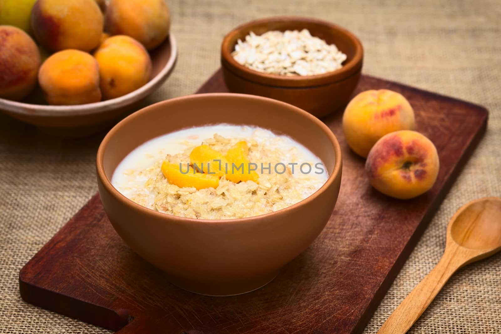 Bowl of oatmeal porridge served with peach slices photographed with natural light (Selective Focus, Focus on the front of the peach slices)