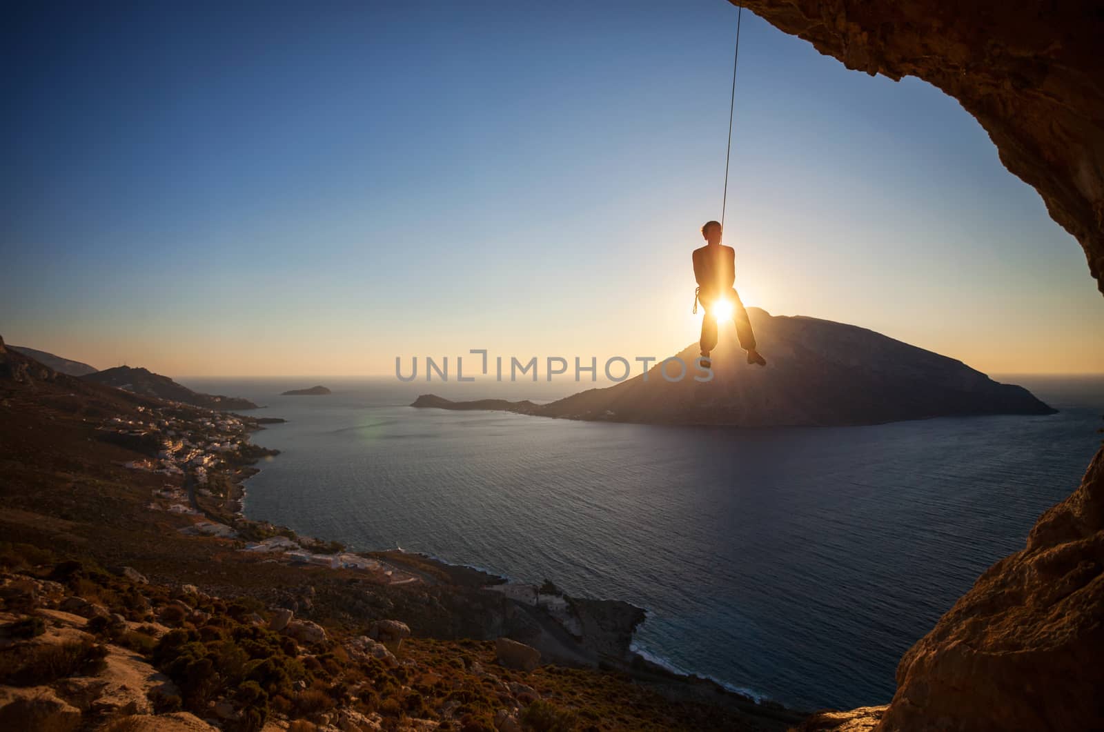 Rock climber hanging on rope while lead climbing at sunset, with Telendos island in background. Kalymnos island, Greece.