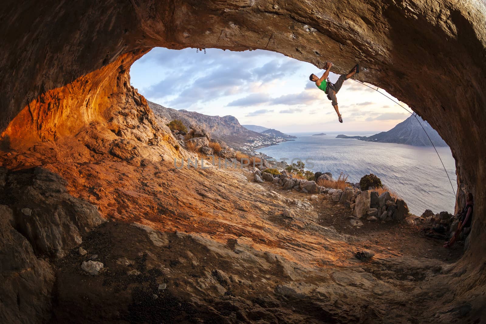 Male rock climber climbing along a roof in a cave by photobac