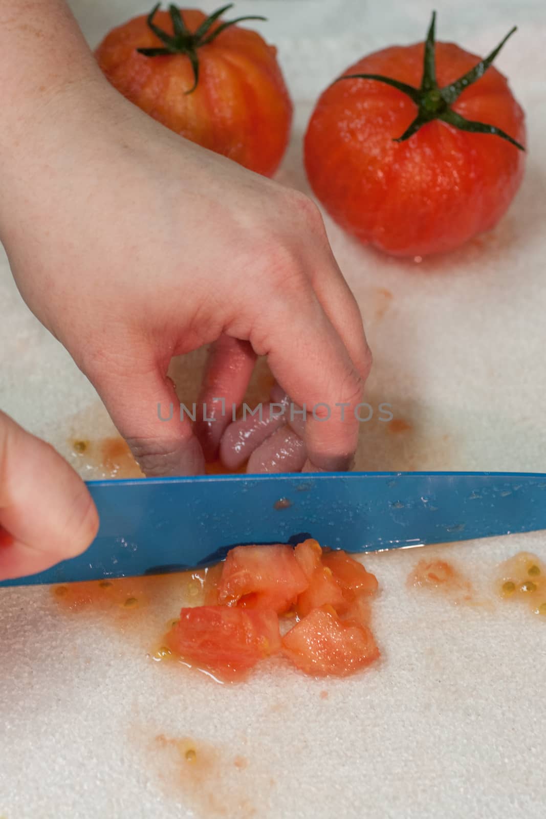 Fresh tomatoes being diced on a cutting board by a female chef with a ceramic knife.