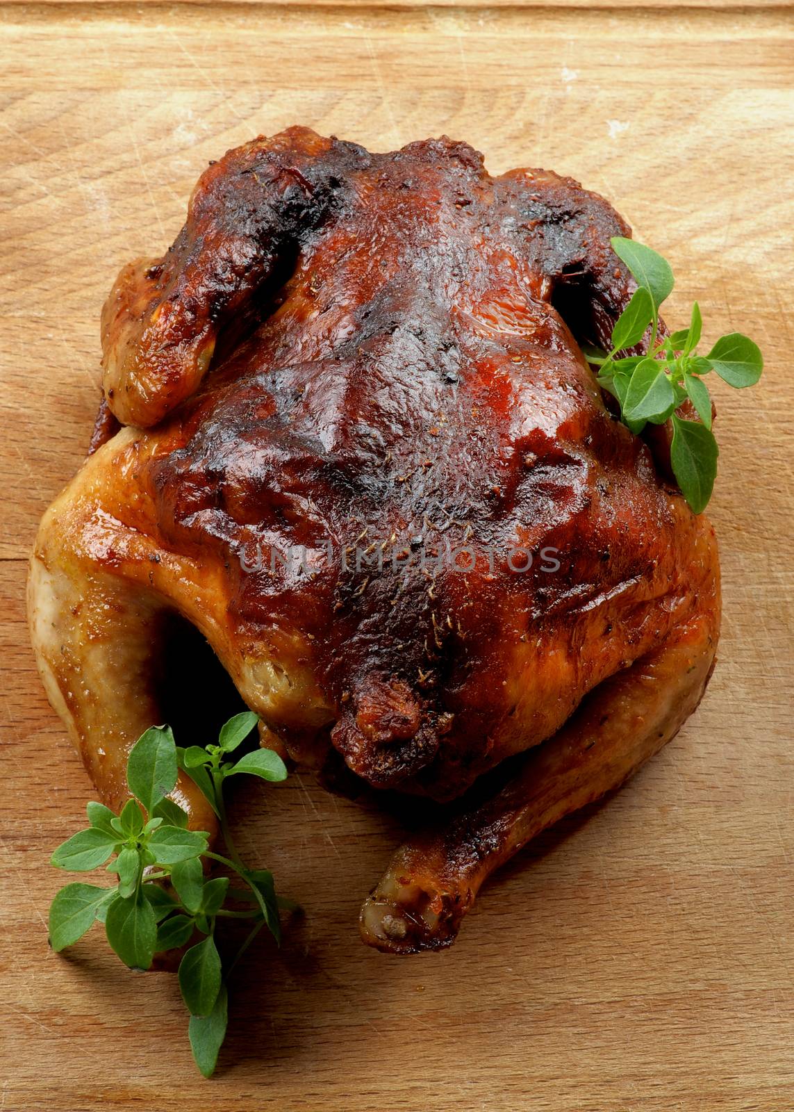 Whole Roasted Chicken with Fresh Basil Leafs closeup on Wooden Cutting Board