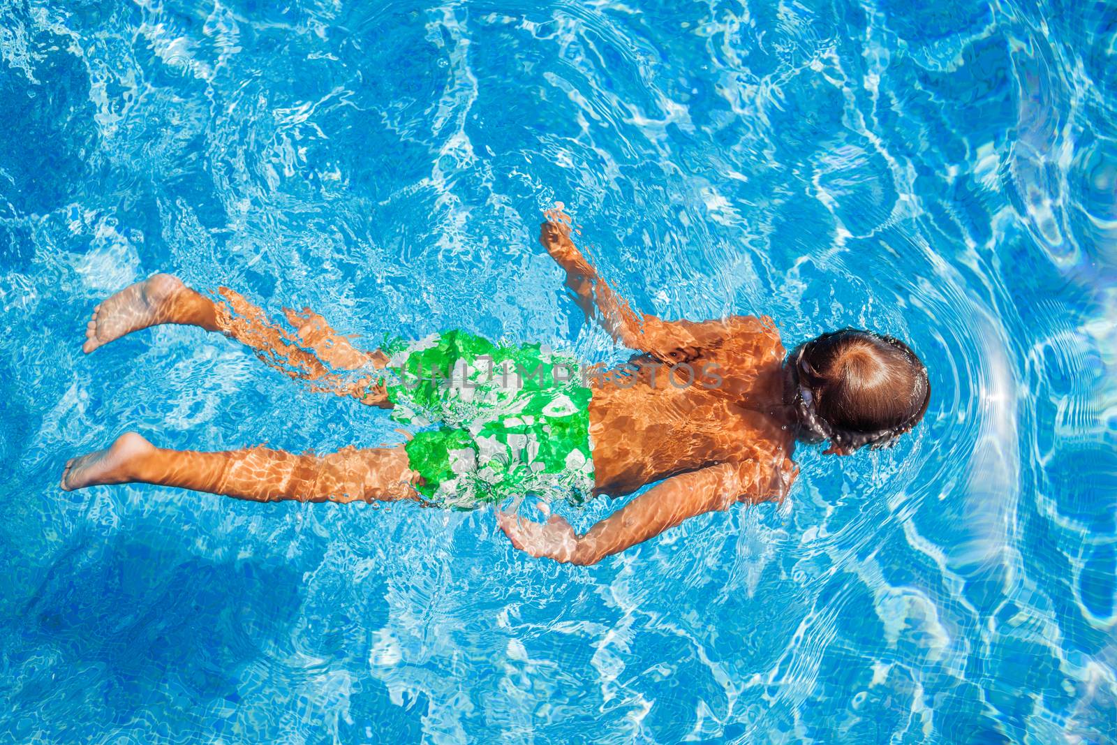 Cute happy little boy in goggles swimming and snorking in the swimming pool