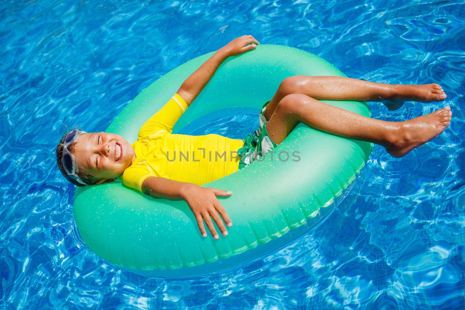 Cute little boy swims in a pool in an green life preserver