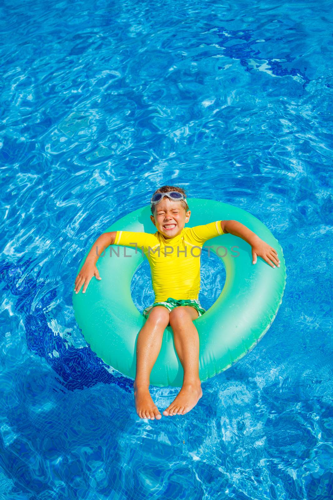 Cute little boy swims in a pool in an green life preserver