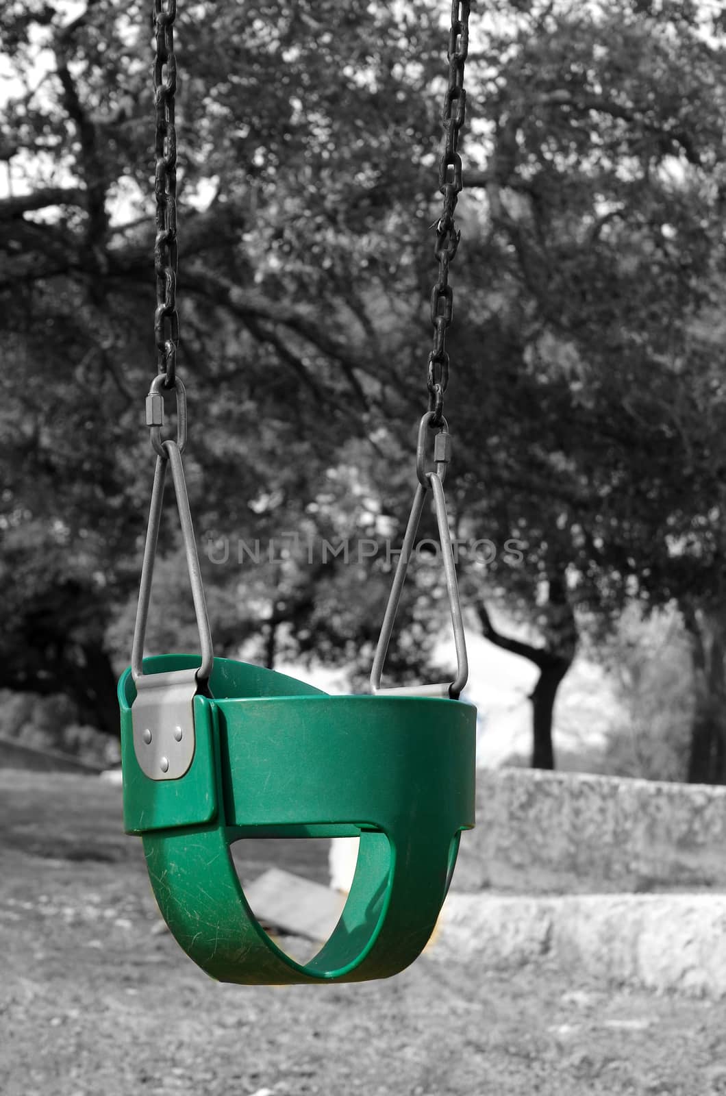 A green infant's swing hangs stationary and empty in a park