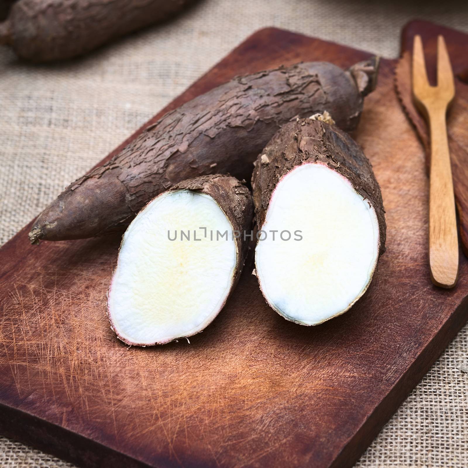 Cut manioc halves (lat. Manihot esculenta) on wooden board photographed with natural light (Selective Focus, Focus on the cut maniocs)