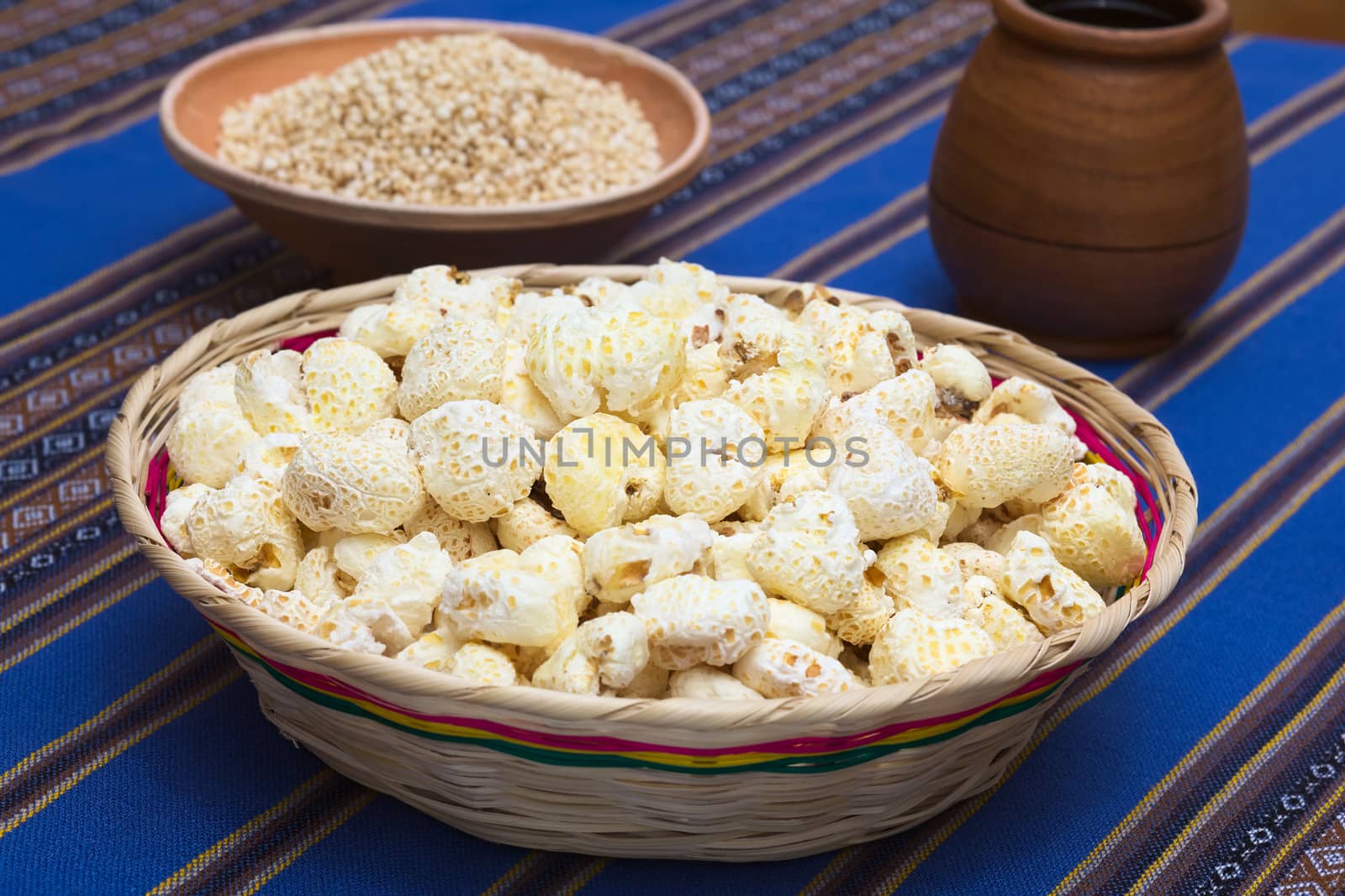 Sweetened popped white corn called Pasancalla eaten as snack in Bolivia served in a woven basket with coca tea in the back, photographed with natural light (Selective Focus, Focus in the middle of the snack) 
   