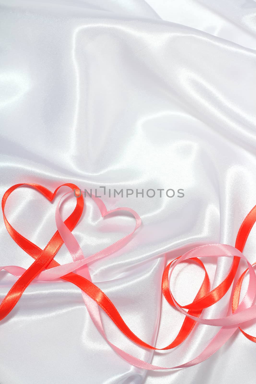 Red and pink satin glossy ribbon hearts over white silk background