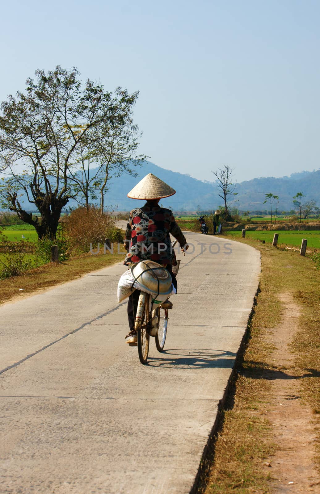 BUON ME THUOT, VIET NAM- FEB 7: Vietnamese woman riding bicycle on country road, beautiful of natural landscape at Daklak countryside, Vietnam, Feb 7, 2014