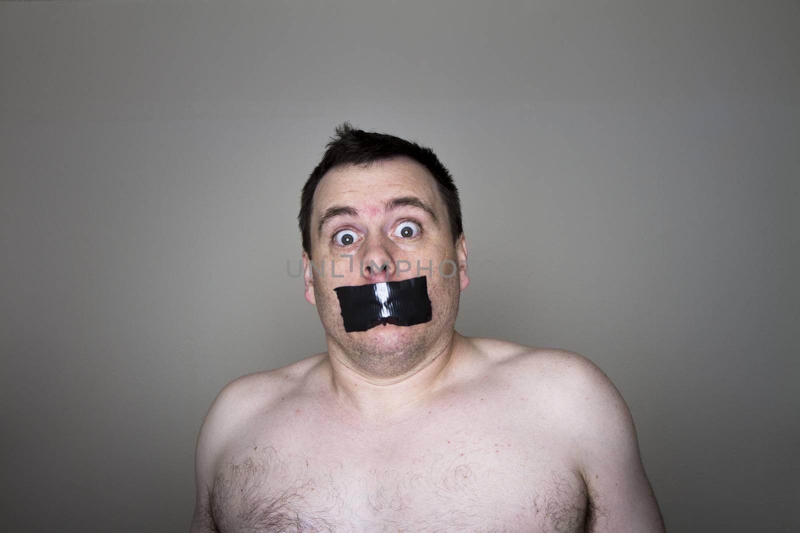 Man topless and having tape over his mouth being held against his will