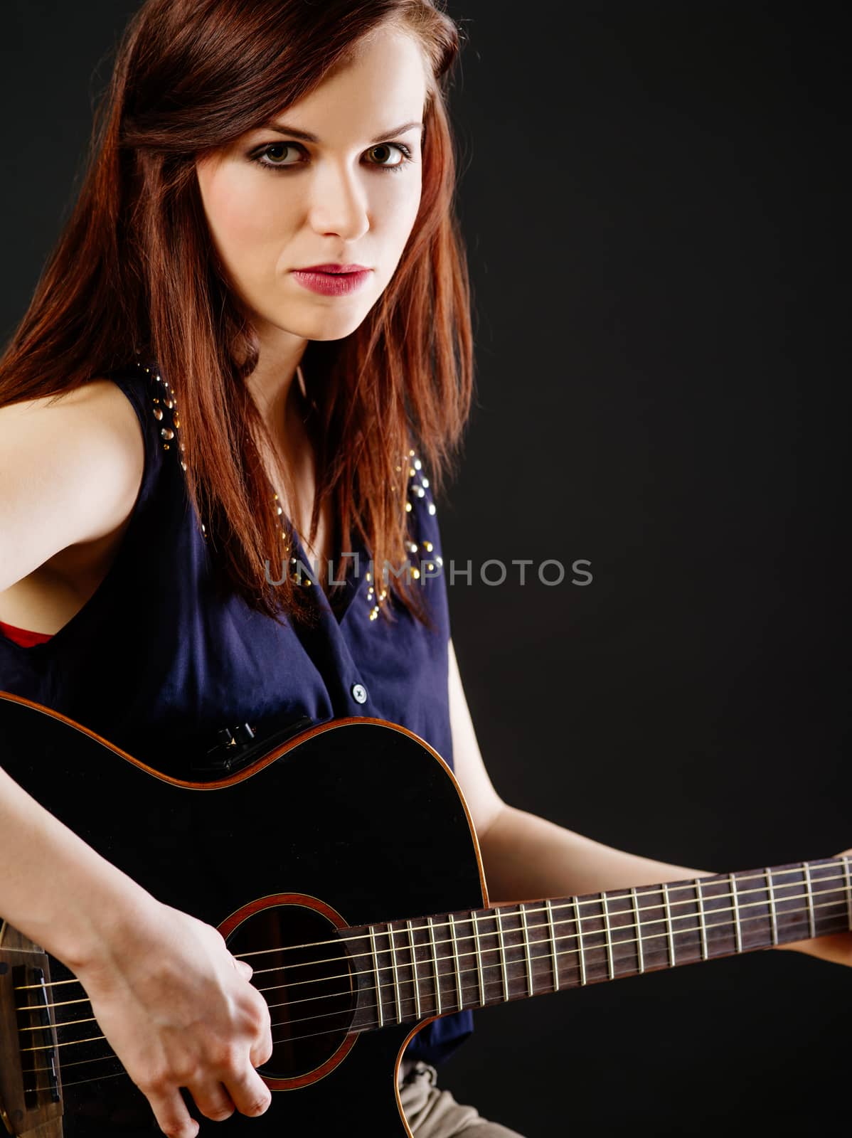 Photo of a beautiful brunette female playing an acoustic guitar over black background.
