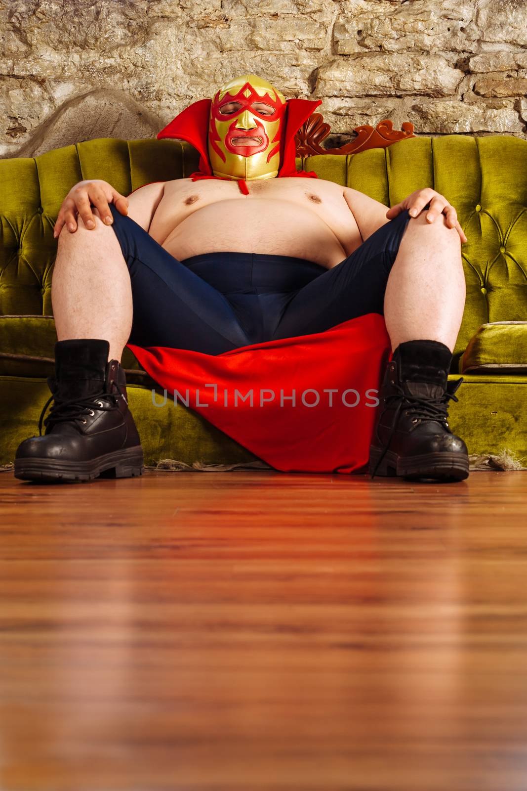 Photograph of a Mexican wrestler or Luchador sitting on a green couch waiting for his match to begin.