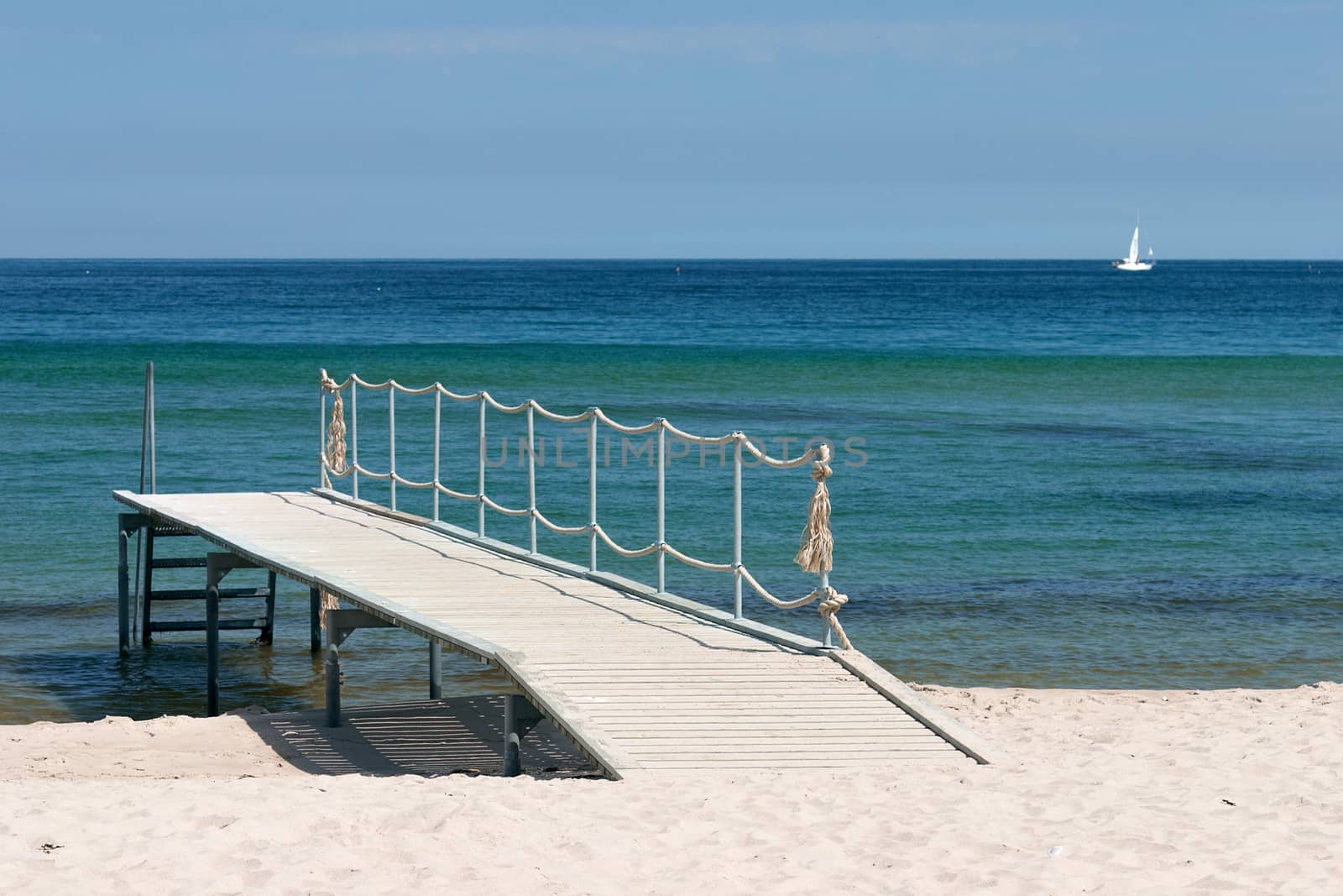 Wooden pier on the sandy beach over the green sea