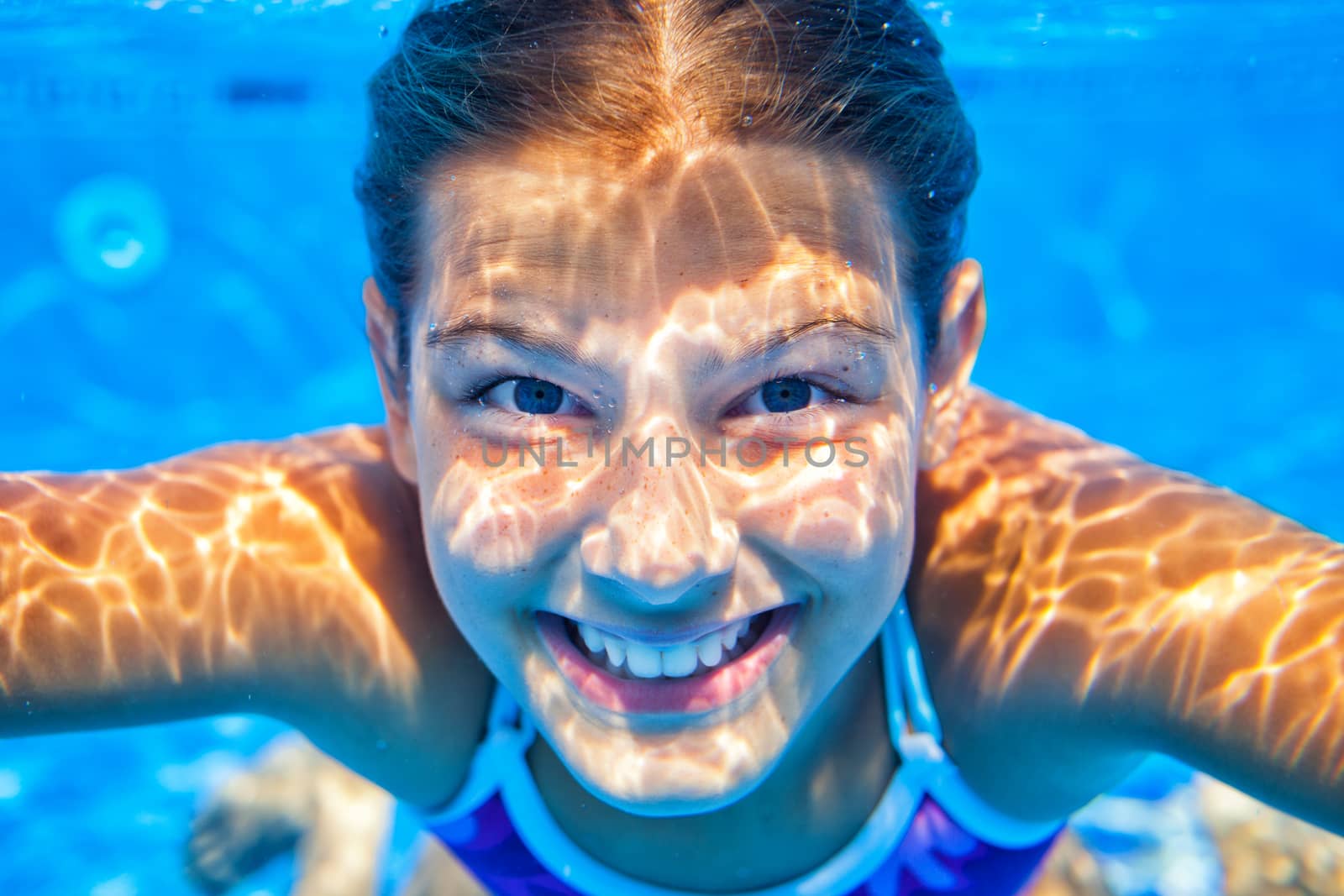 Close-up portrait of underwater happy cute girl in swimming pool