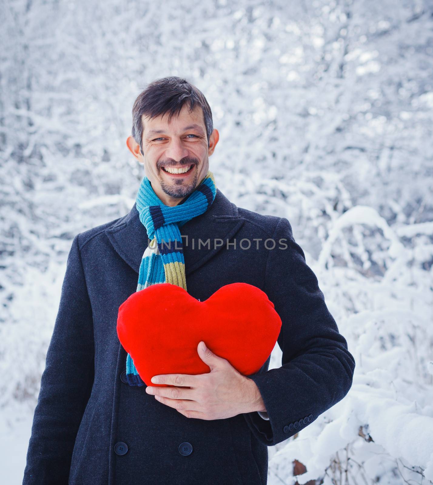 Man holding red heart in his hands in winter forest