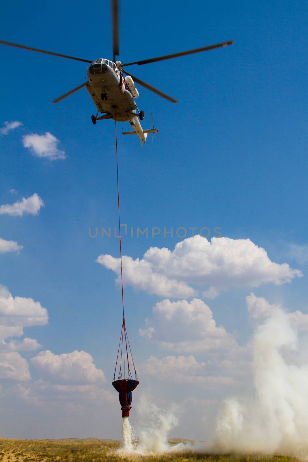 Firefighting helicopter attacks a wildfire with a cascading water release from its water bucket.