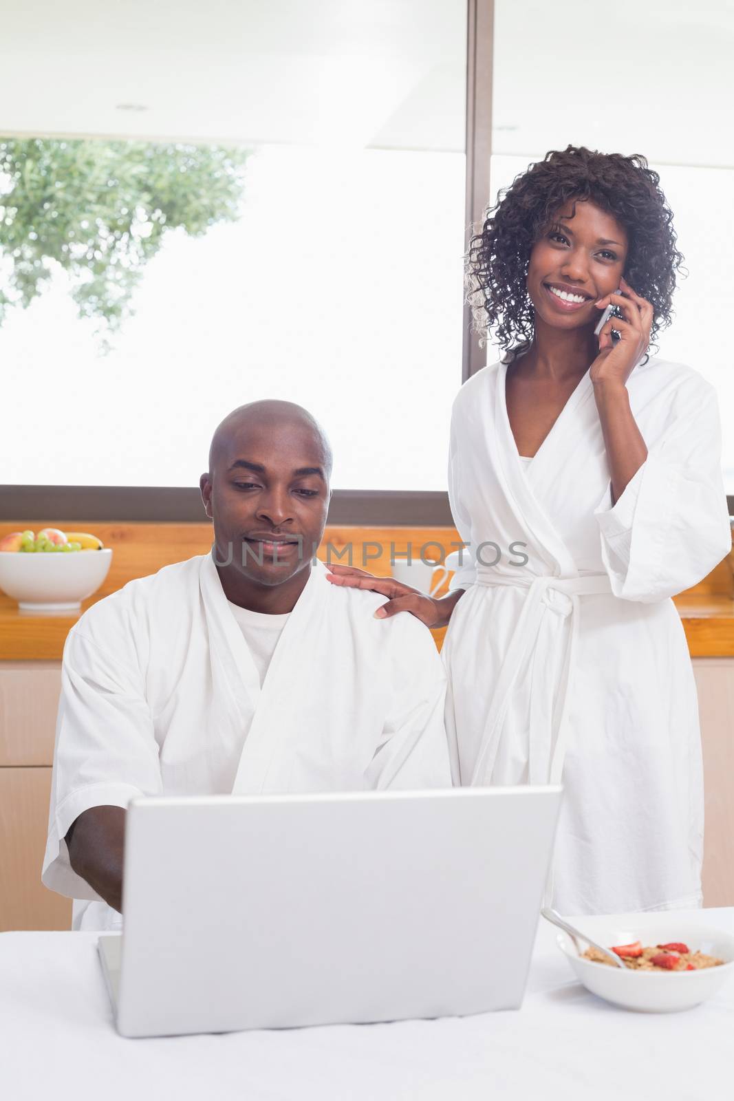 Happy couple in bathrobes in the kitchen using technology at home in the kitchen