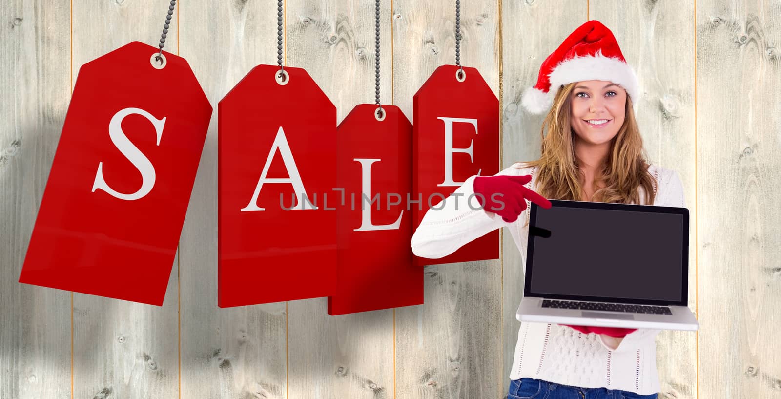 Festive blonde pointing to laptop against pale wooden planks
