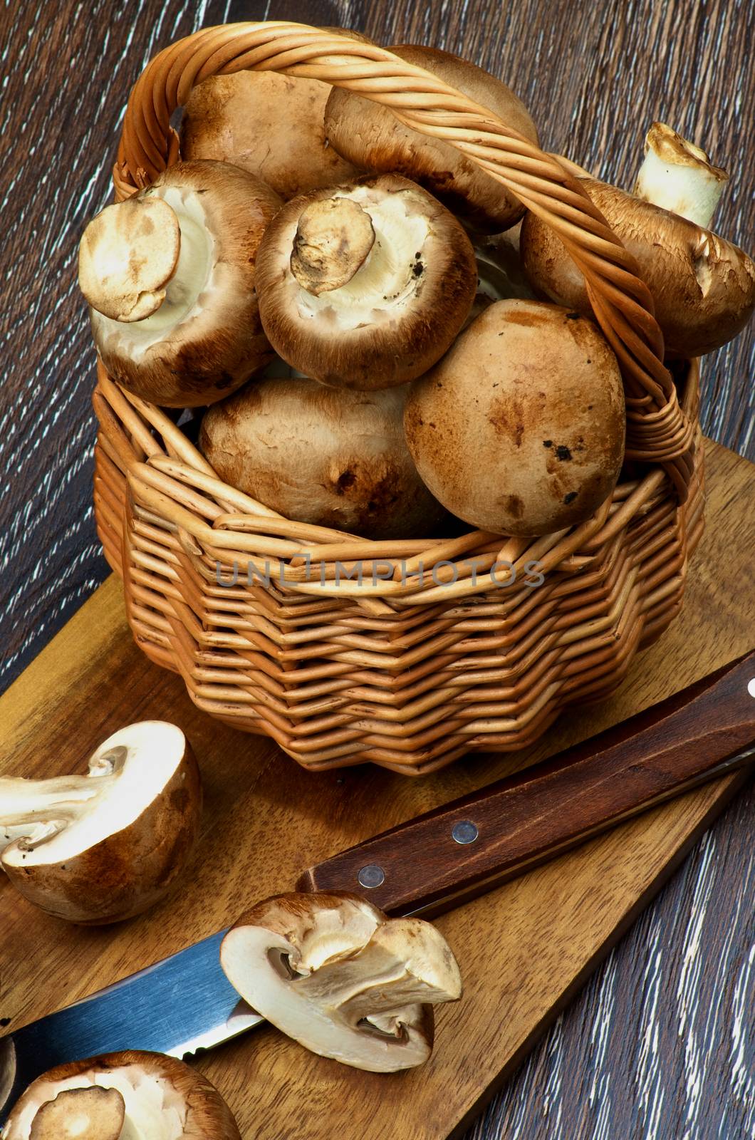 Gourmet Raw Portabello Mushrooms Full Body and Halves in Wicker Basket with Table Knife on Cutting Board closeup on Dark Wooden background