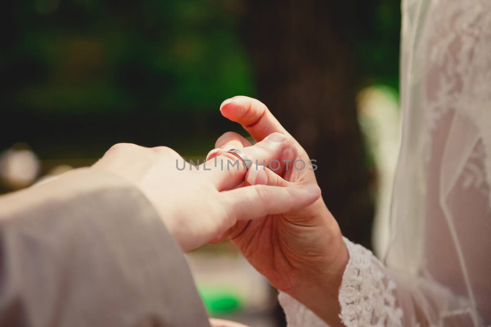 mans hand putting a wedding ring on the brides finger by sarymsakov