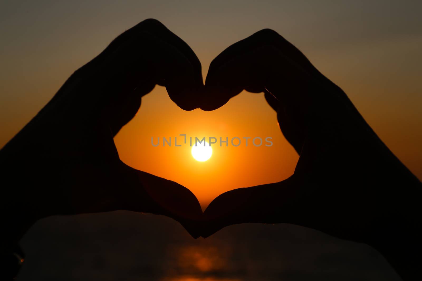 Silhouettes hand heart shaped with sun sets and the sky orange