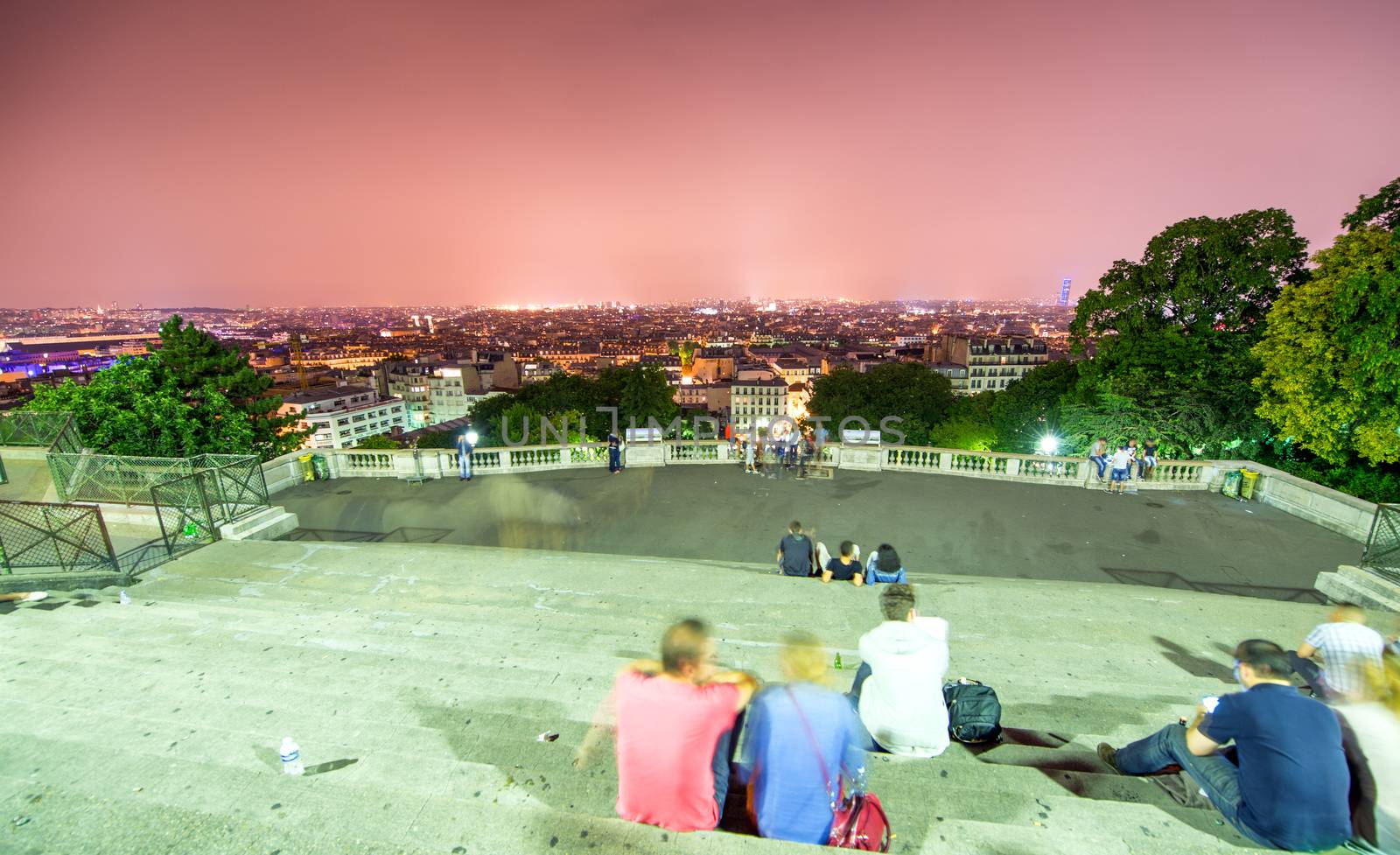 Tourists in Montmartre steps enjoying Paris night skyline.