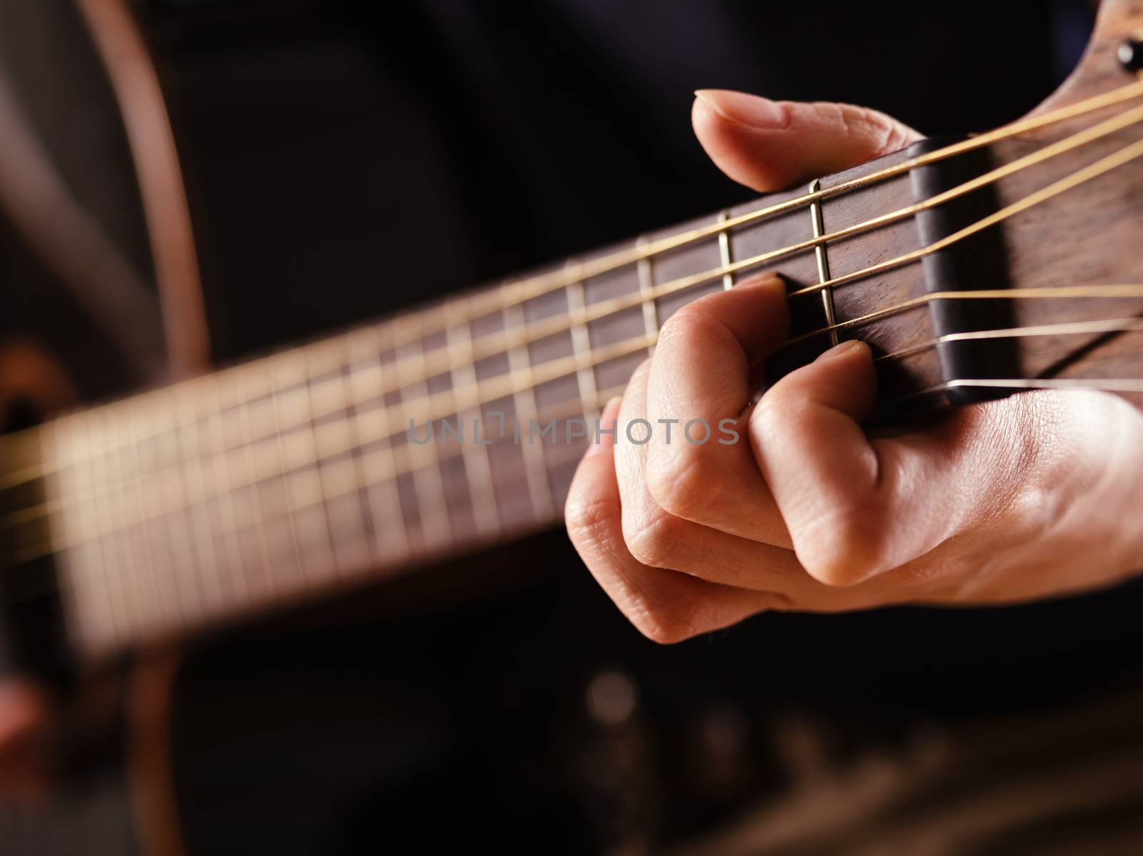 Photo of a woman playing an acoustic guitar with extreme shallow depth of field with focus on hand and headstock.