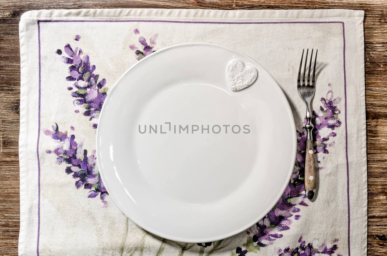 Plate and fork laid on vintage wooden dining table with colorful tablecloth