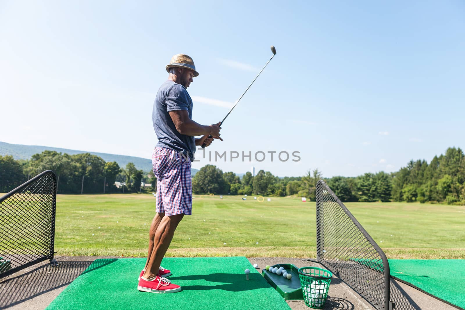 Athletic golfer teeing up at the driving range dressed in casual attire.