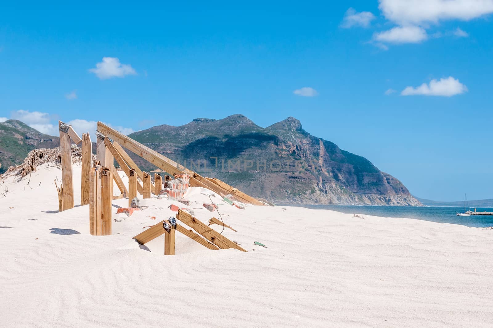 Old police station at Hout Bay reclaimed by sand dunes, Cape Town, South Africa. Sand grains swept into the air is visible over the sea

