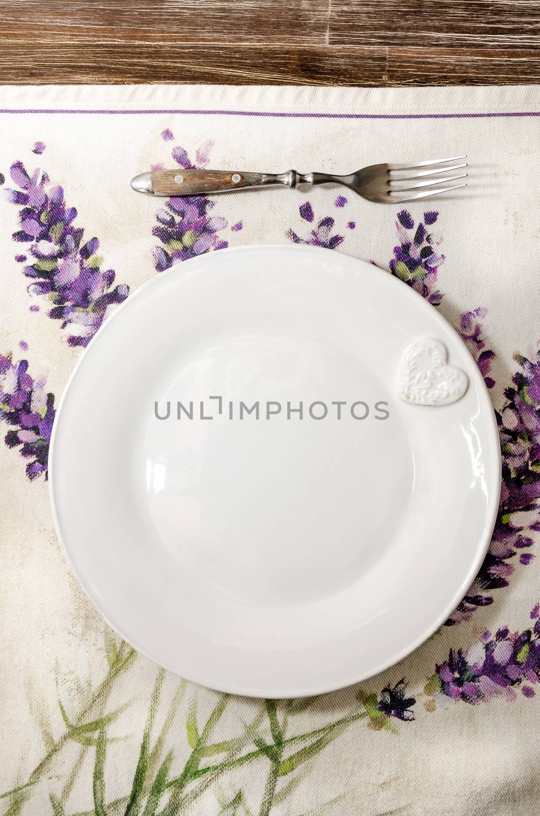 Fork and plate laid on vintage wooden dining table with colorful tablecloth