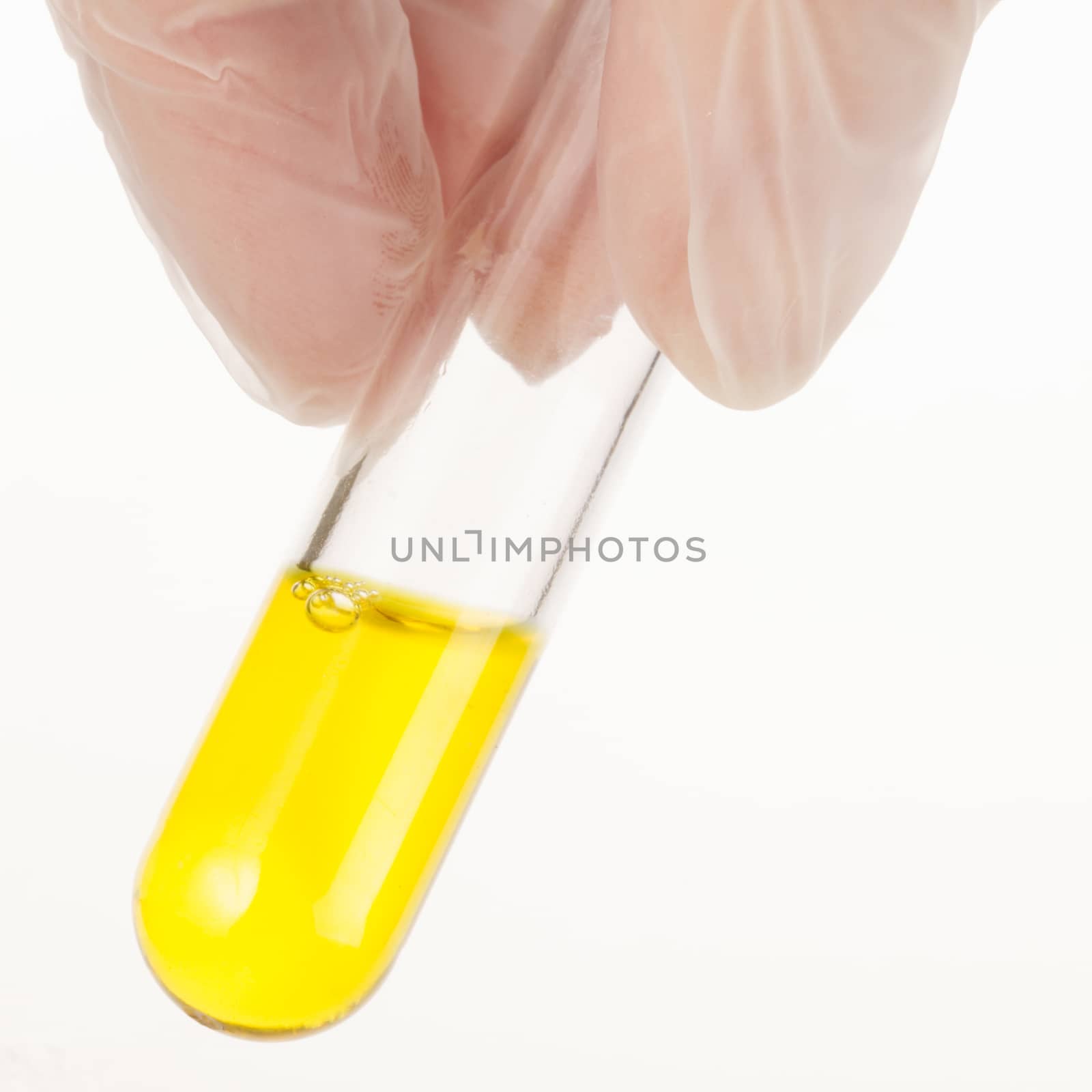 Fingers holding test tube with yellow liquid.