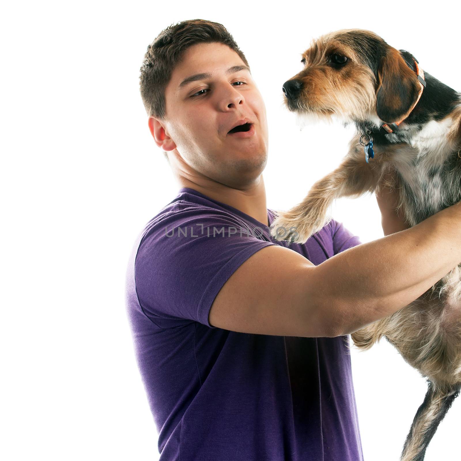 High key portrait of a young man holding a cute mixed breed dog isolated over white. 