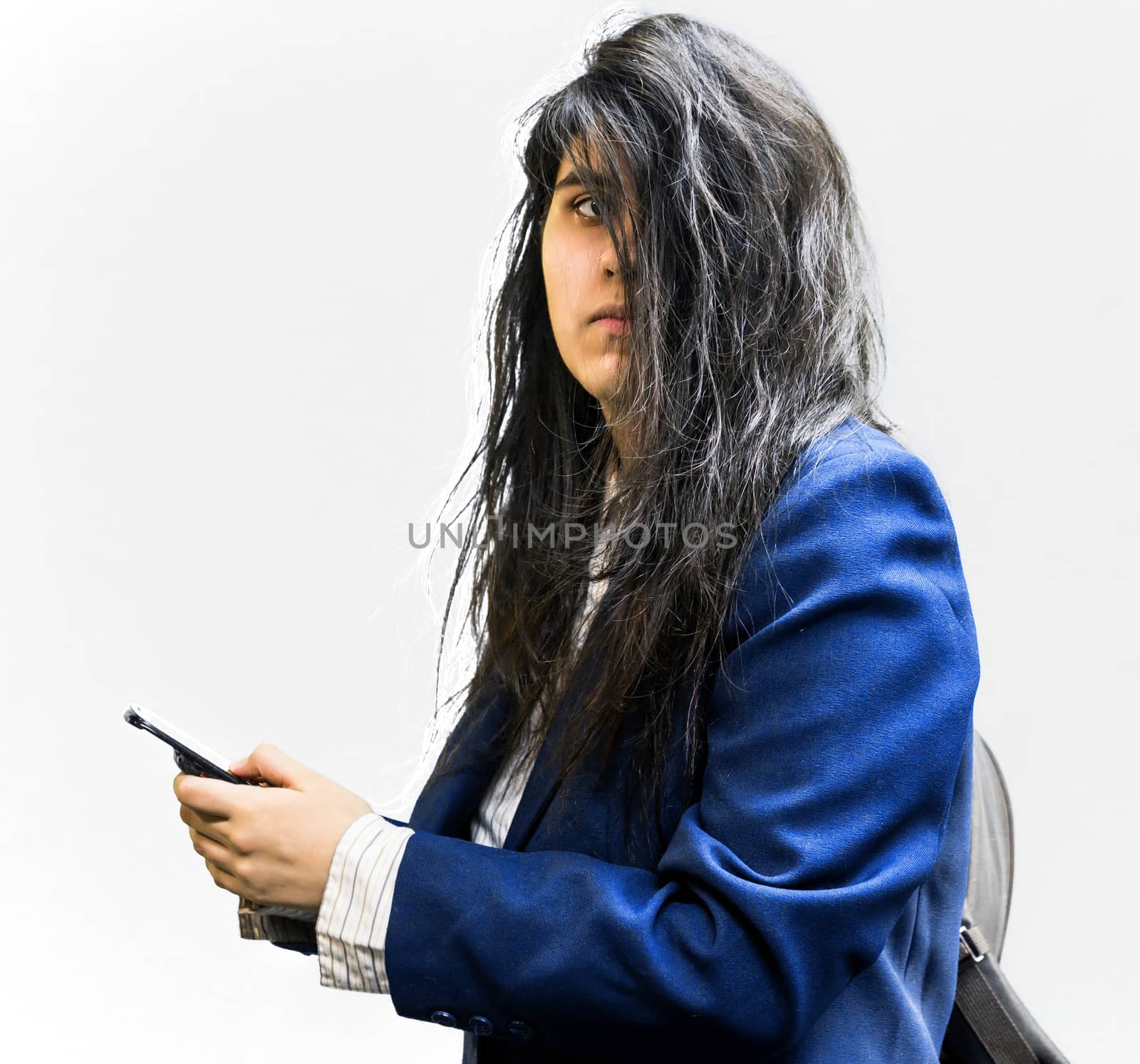 Side shot of latina teen girl with a backpck on, holding a cellphone, and looking of to the side