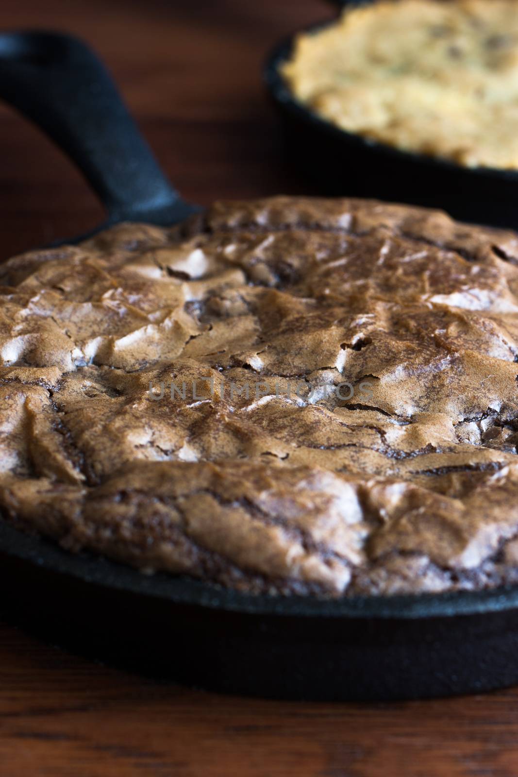 Brownies in a cast iron pan with chocolate chip cookies in the back ground.