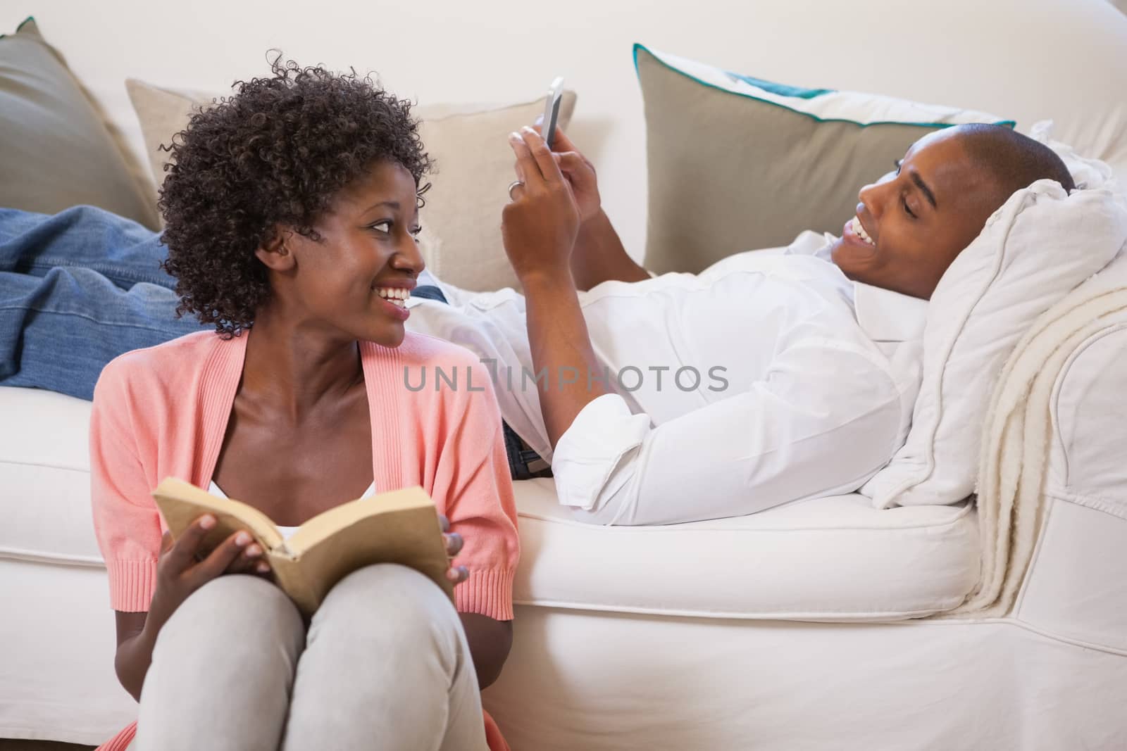 Happy couple relaxing together reading book and using smartphone by Wavebreakmedia