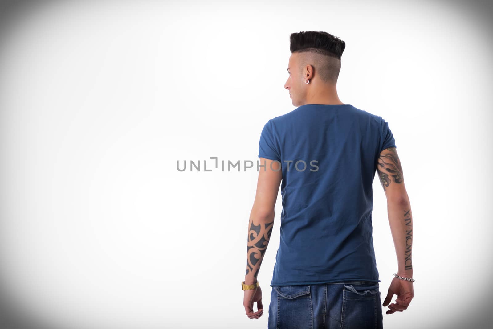 Back of trendy young man looking to a side at empty copy space, wearing blue t-shirt and jeans