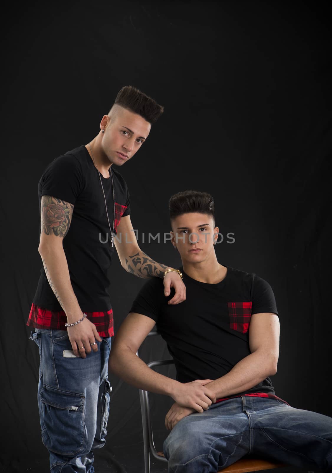 Two hip trendy male friends in studio shot, one is sitting on a chair
