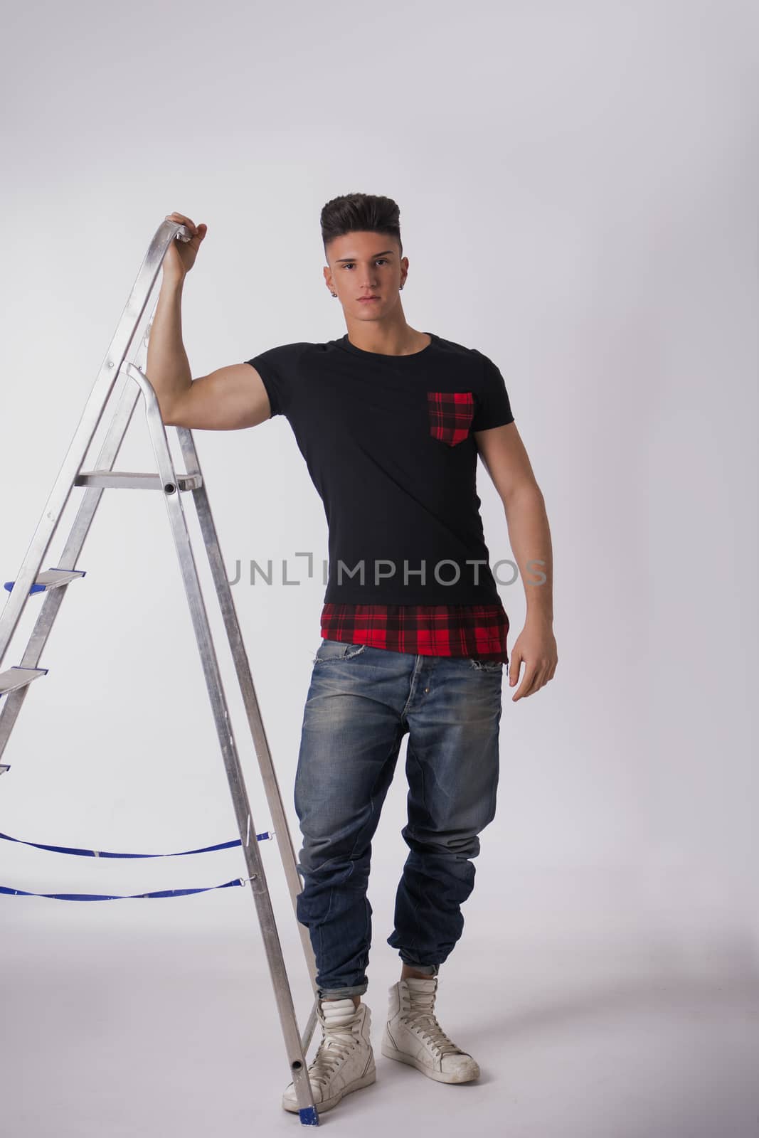 Attractive young man leaning on metal ladder, looking at camera, on white background