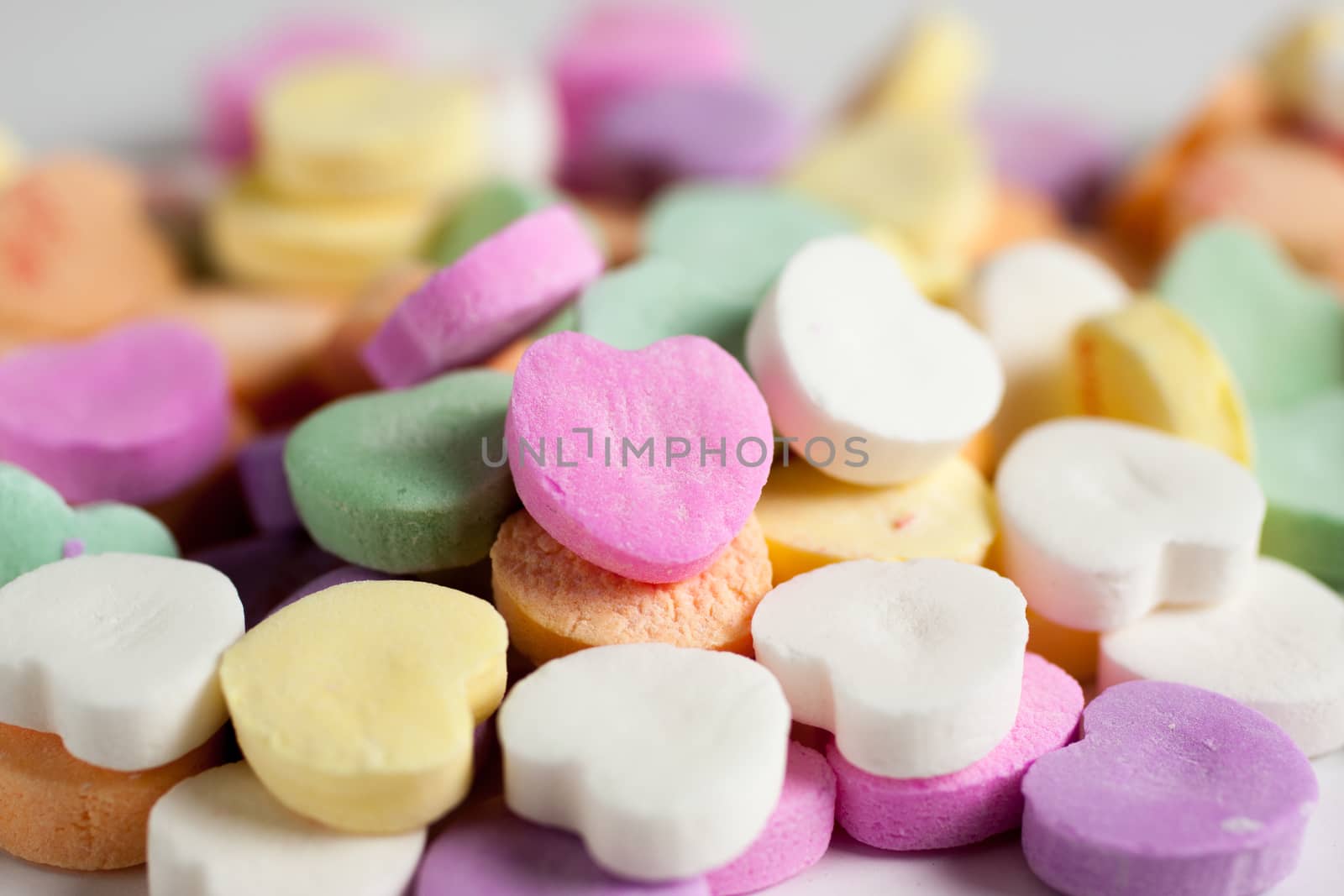 Pastel colored candy hearts in a pile on a white surface.