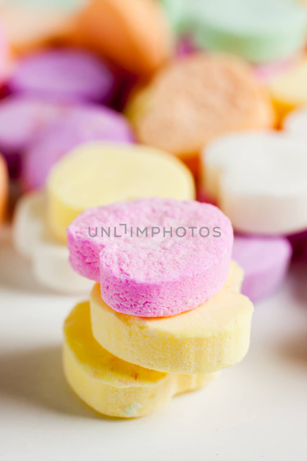 Pastel colored candy hearts in a pile on a white surface.