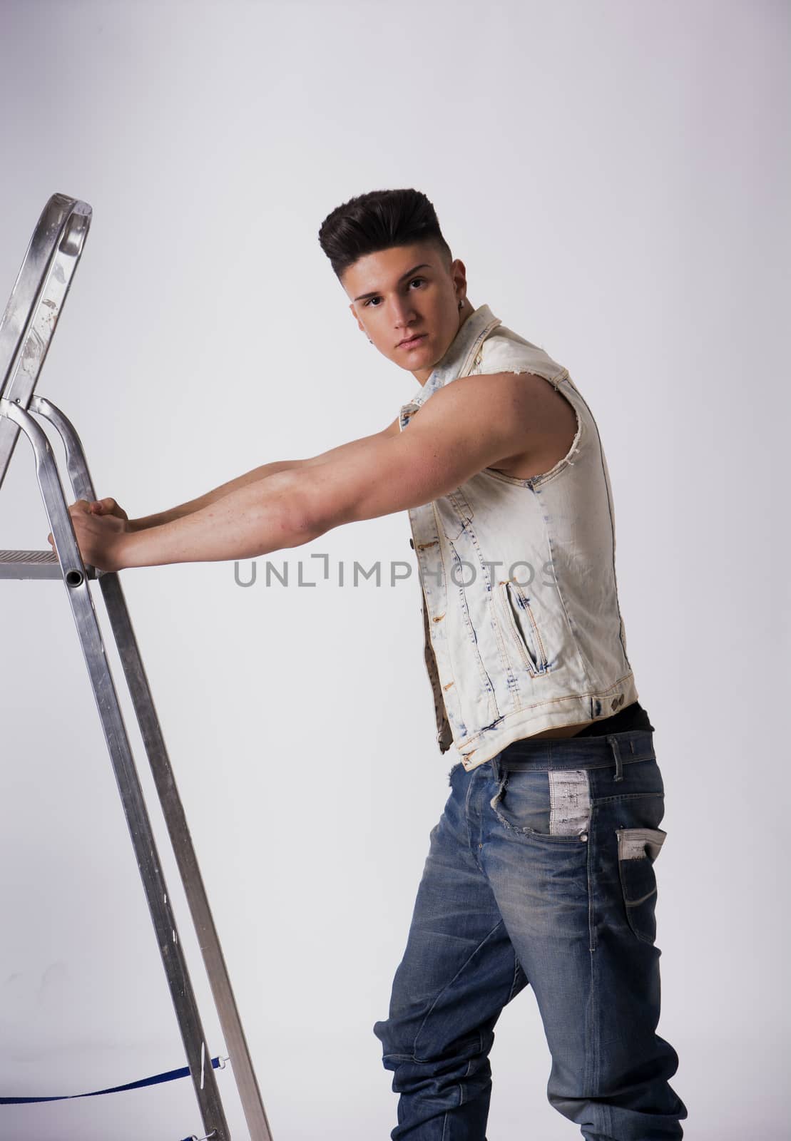 Attractive young man leaning on metal ladder, looking at camera, on white background