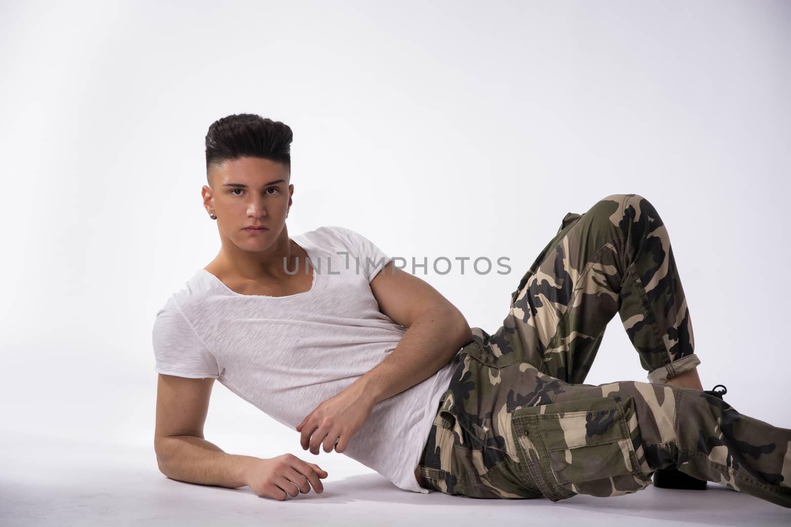 Handsome young man laying down on floor wearing camouflage pants, white background