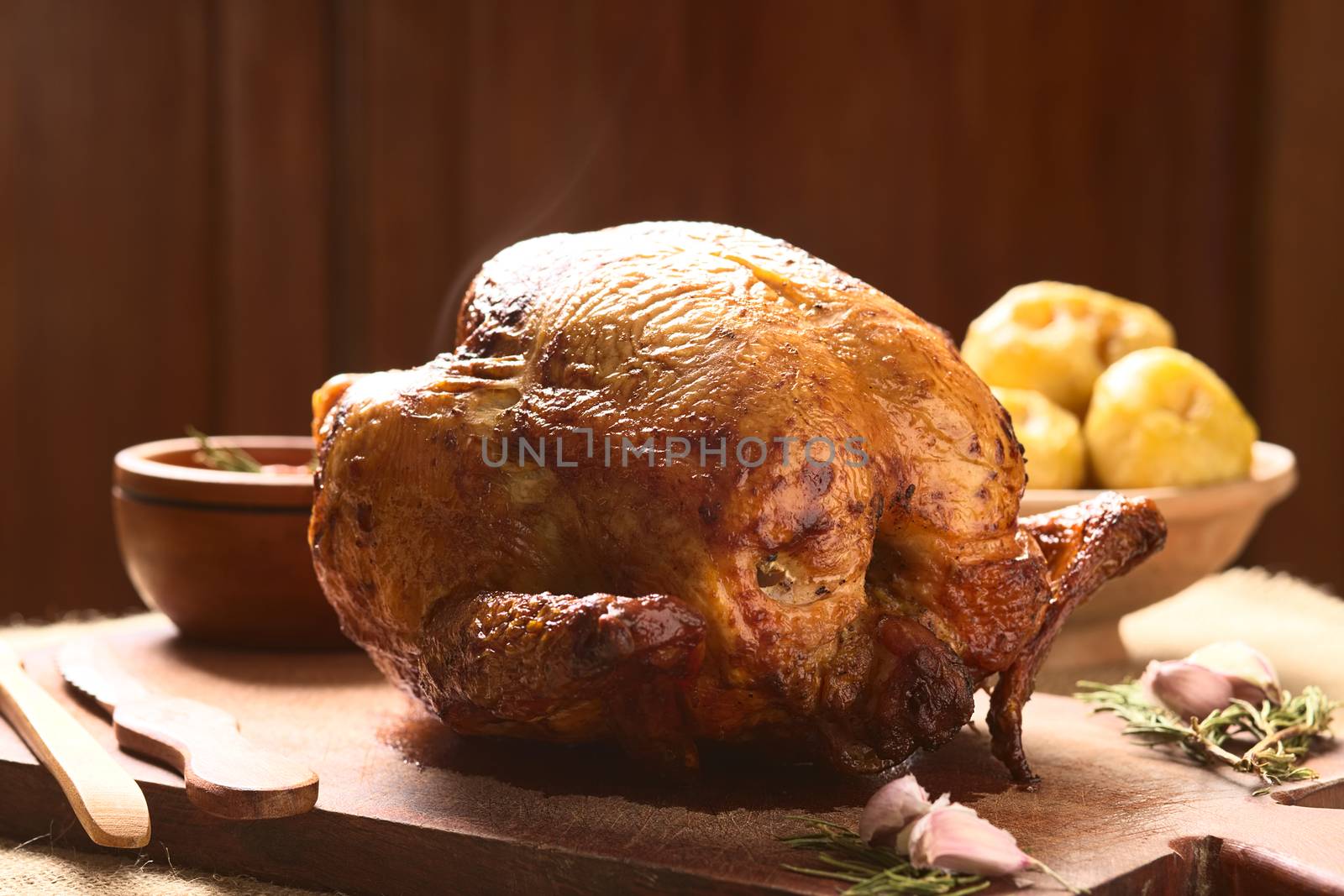 Roast Chicken on wooden board with spices, potatoes in the back, photographed with natural light (Selective Focus, Focus on the front of the breast)  