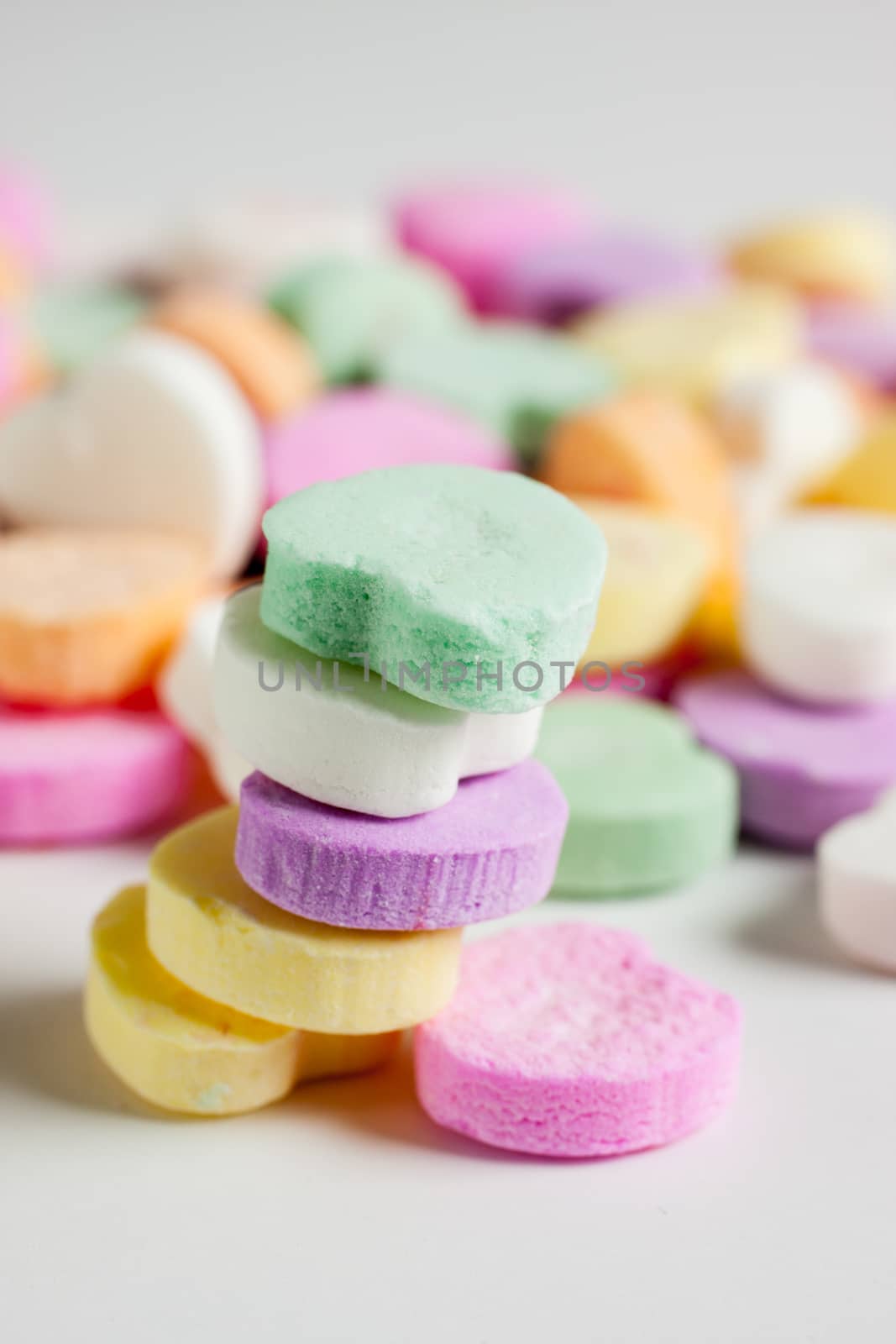 Pastel colored candy hearts in a pile on a white surface.