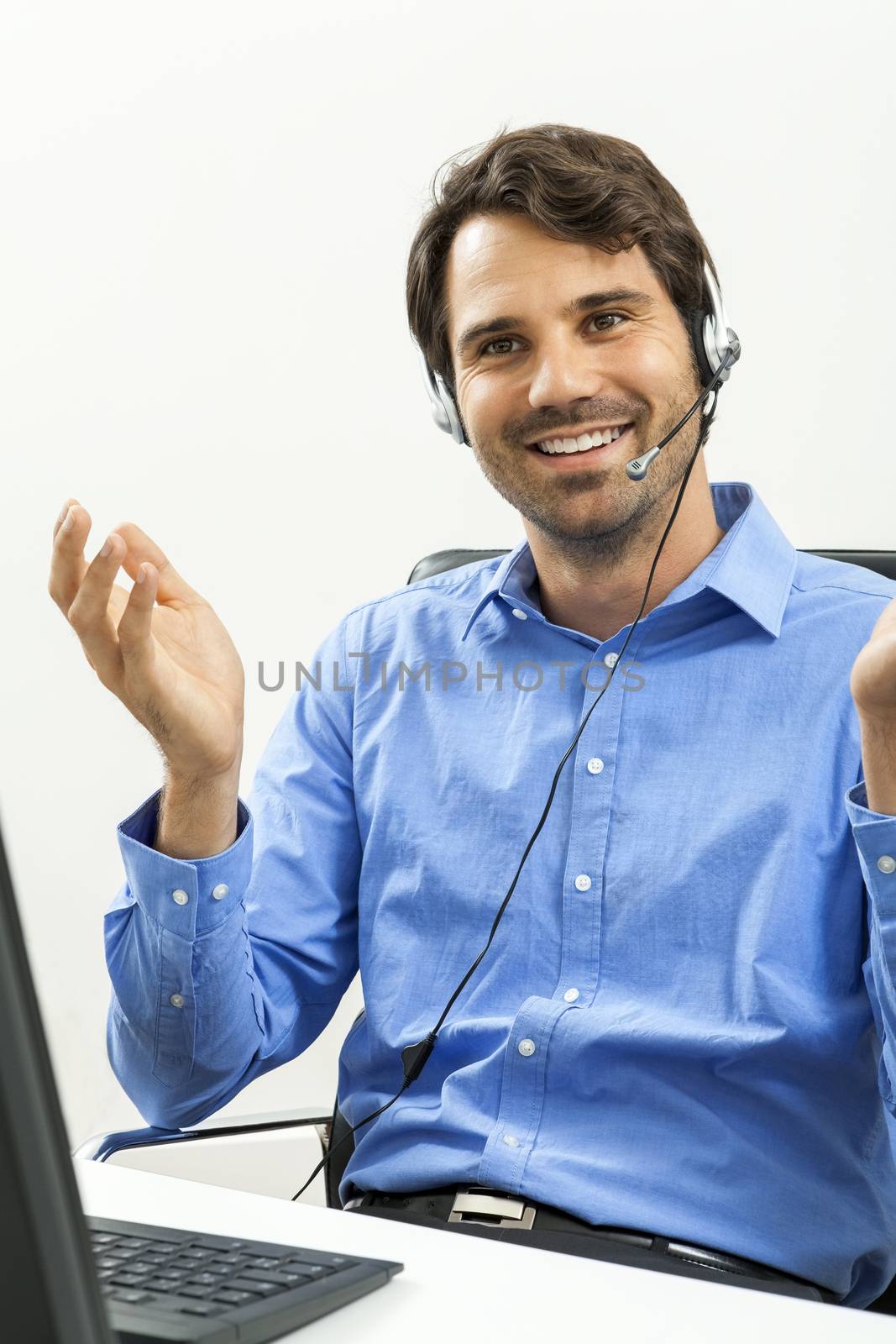 Attractive unshaven young man wearing a headset offering online chat and support on a client services of help desk as he types in information on his computer