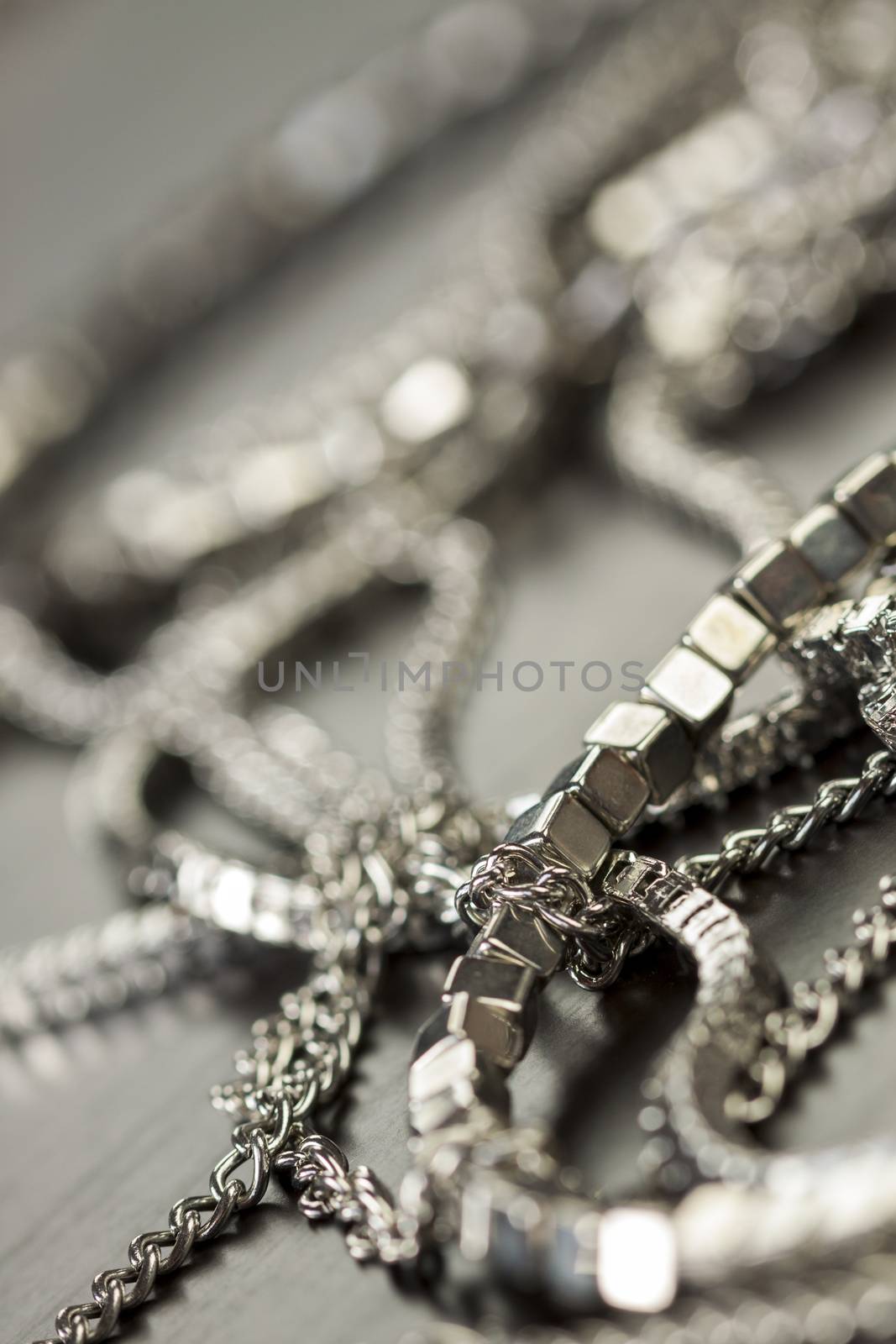 Pile of assorted silver chains with shiny box chains, cube chains and ordinary linked chain on a grey background conceptual of fashion jewellery