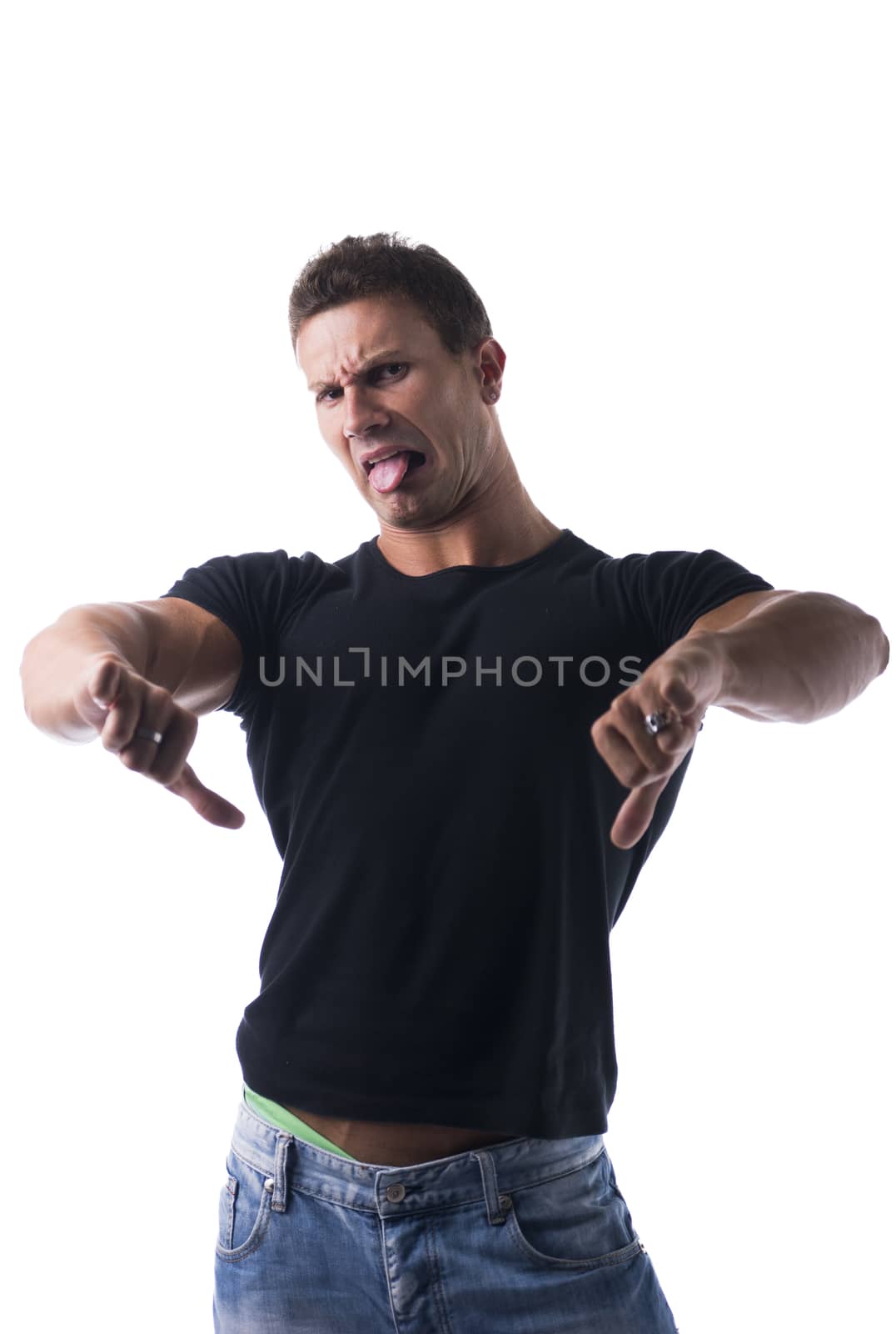 Disgusted young man with funny expression, doing thumbs down gesture and sticking tongue out