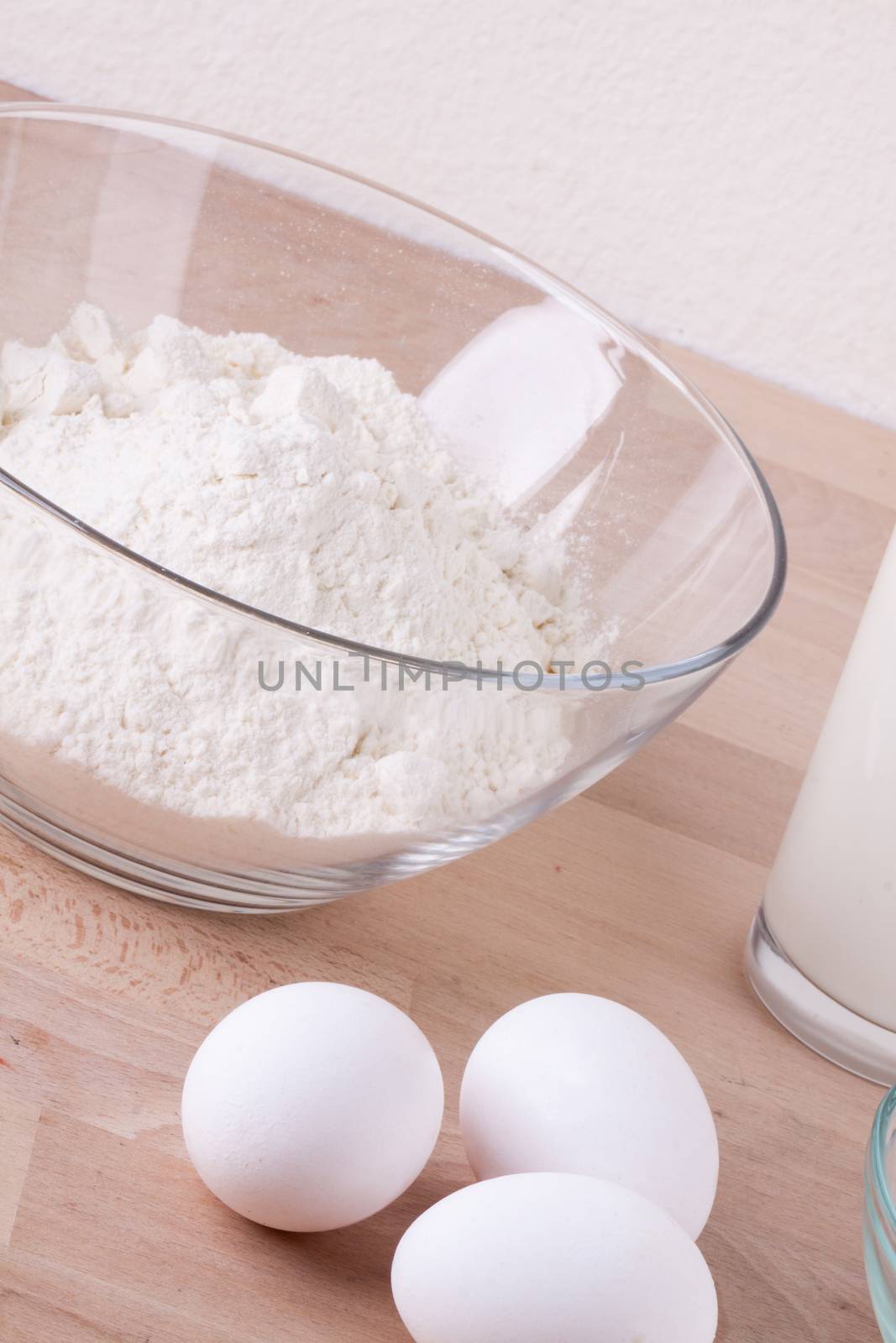 Baking ingredients in the kitchen with a bowl of flour, eggs, sugar, jug of milk and butter ready to bake a cake or make batter