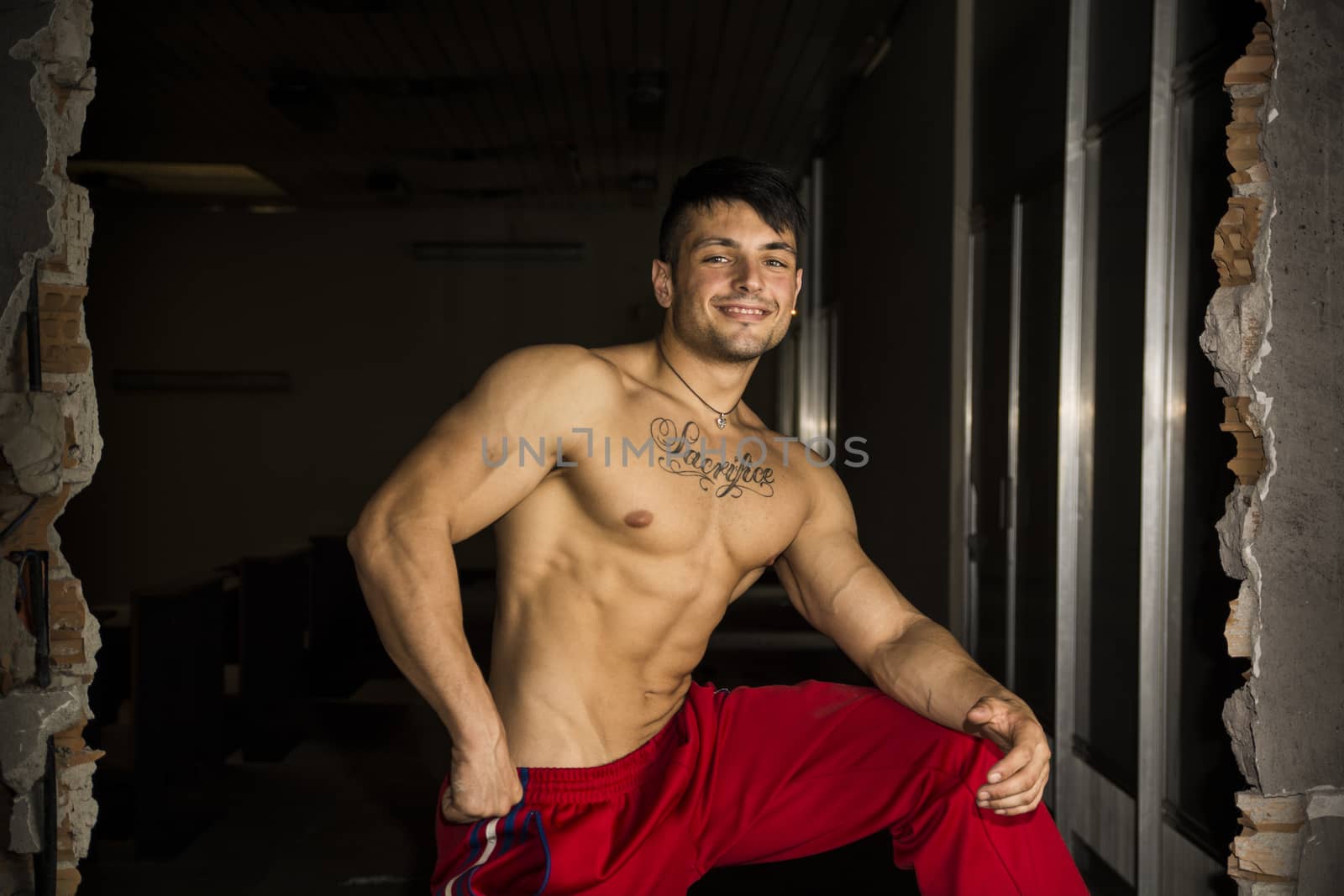 Muscular shirtless young man indoor smiling at camera in abandoned building